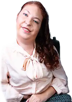 A portrait of Briana Mills outside in front of greenery, sitting in her wheelchair, with her chin restin on the hand facing the camera. She's wearing professional attire with a pink blazer. She is looking at the camera with a confident, comforting smile.
